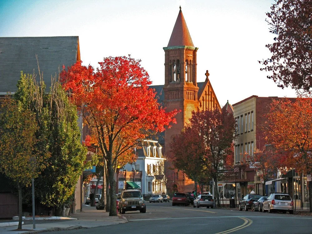 Cabot Street in downtown Beverly, lined with shops beneath autumn foliage and a church steeple.