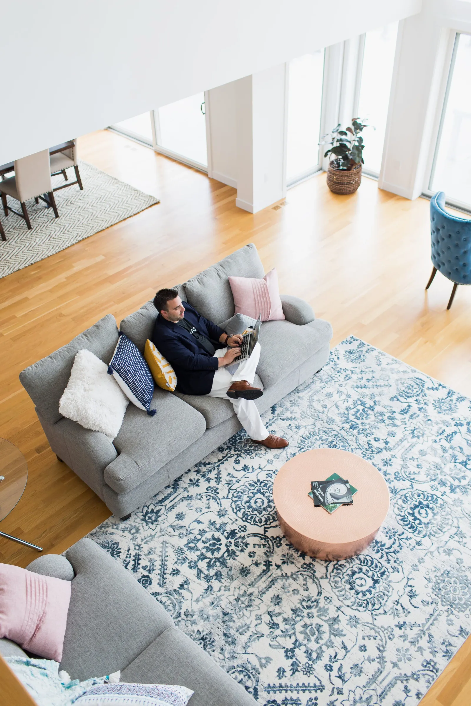 A person working on a laptop on a gray sofa in a bright open-plan living area, reviewing mortgage documents